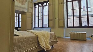 Una habitación con una cama grande, una cama más pequeña, un radiador y una ventana con vista a la calle.