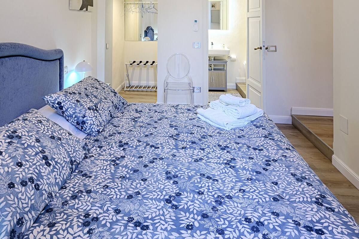 Ein Schlafzimmer mit einem großen Bett, einem Bogen als Durchgang und einem sichtbaren Badezimmer.