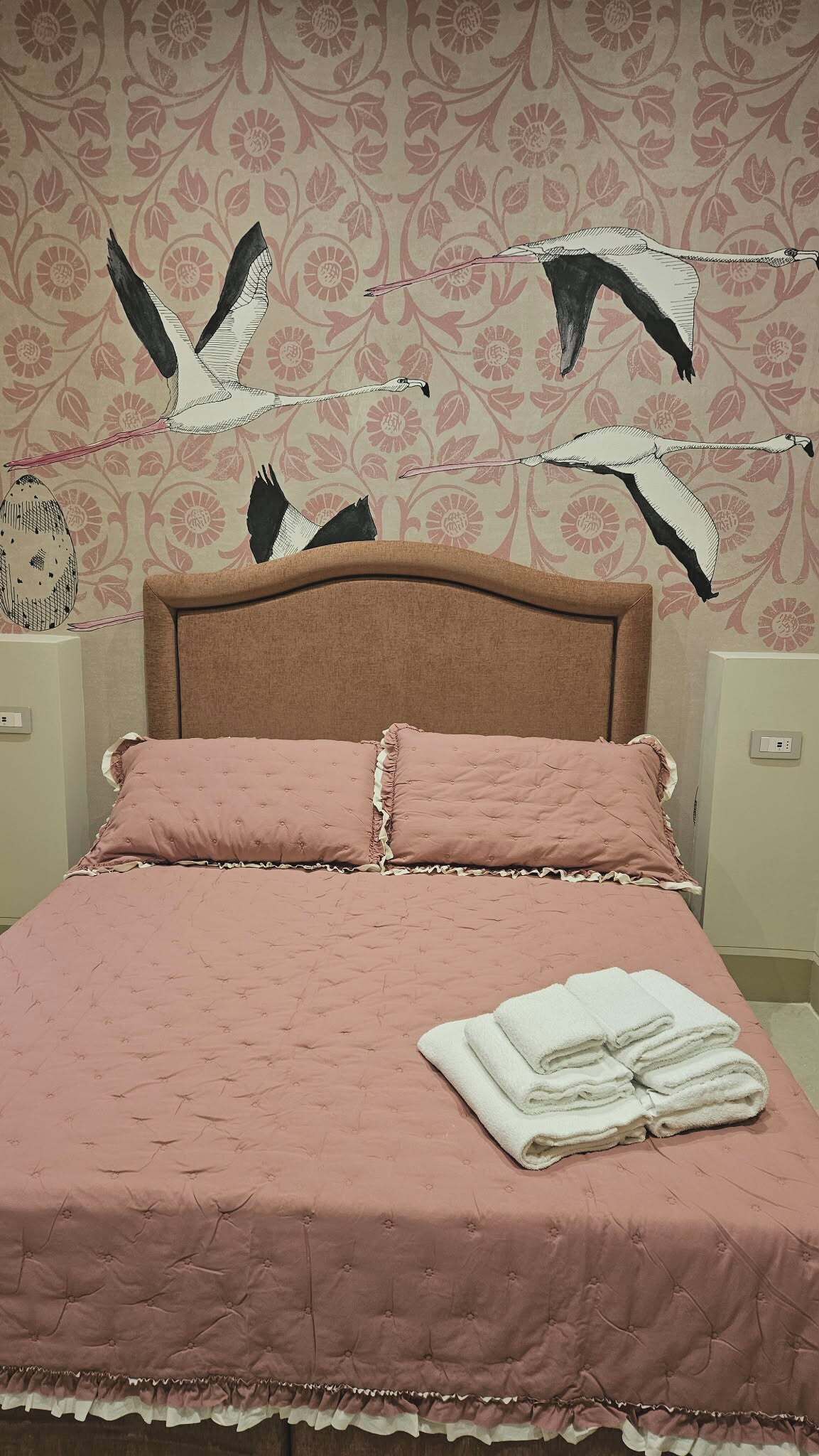 Una cama con un edredón rosa, almohadas blancas y una toalla blanca doblada al lado.