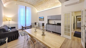 Una cocina moderna con horno integrado, un comedor con mesa y sillas, y una sala de estar con sofá y lámpara.