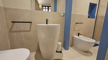 A bathroom with a toilet, a large pedestal sink, and a bidet.