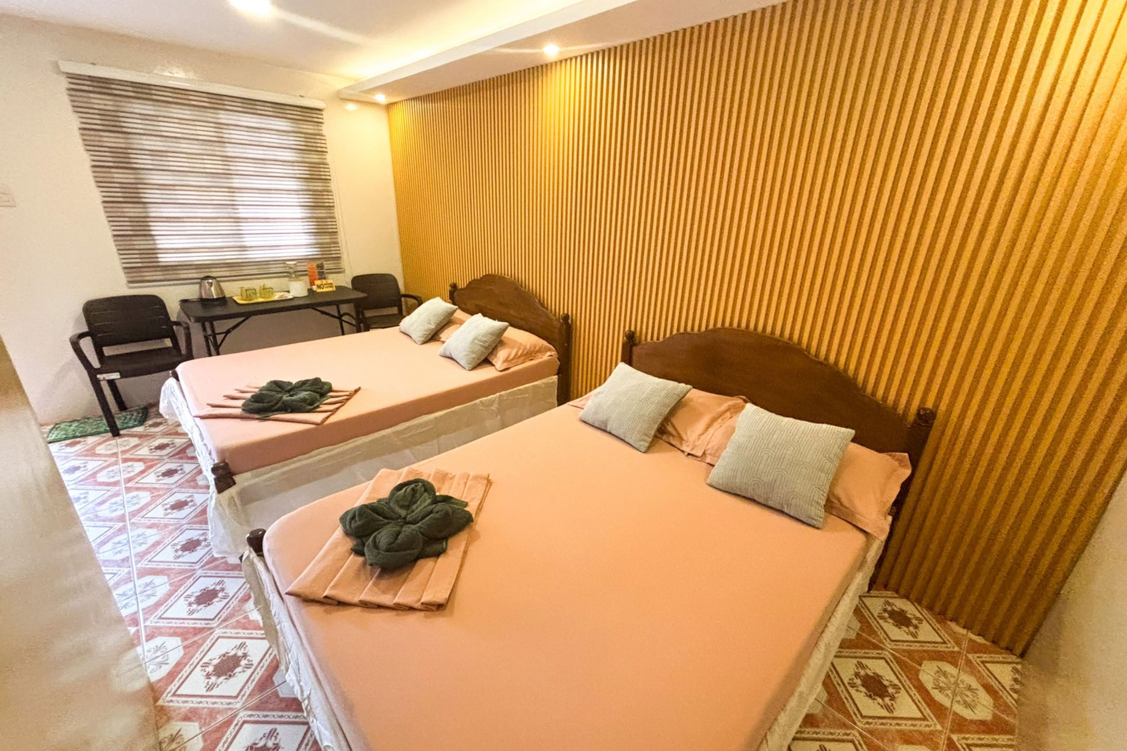 Habitación de hotel con dos camas, un escritorio pequeño con una silla y una ventana con persianas.
