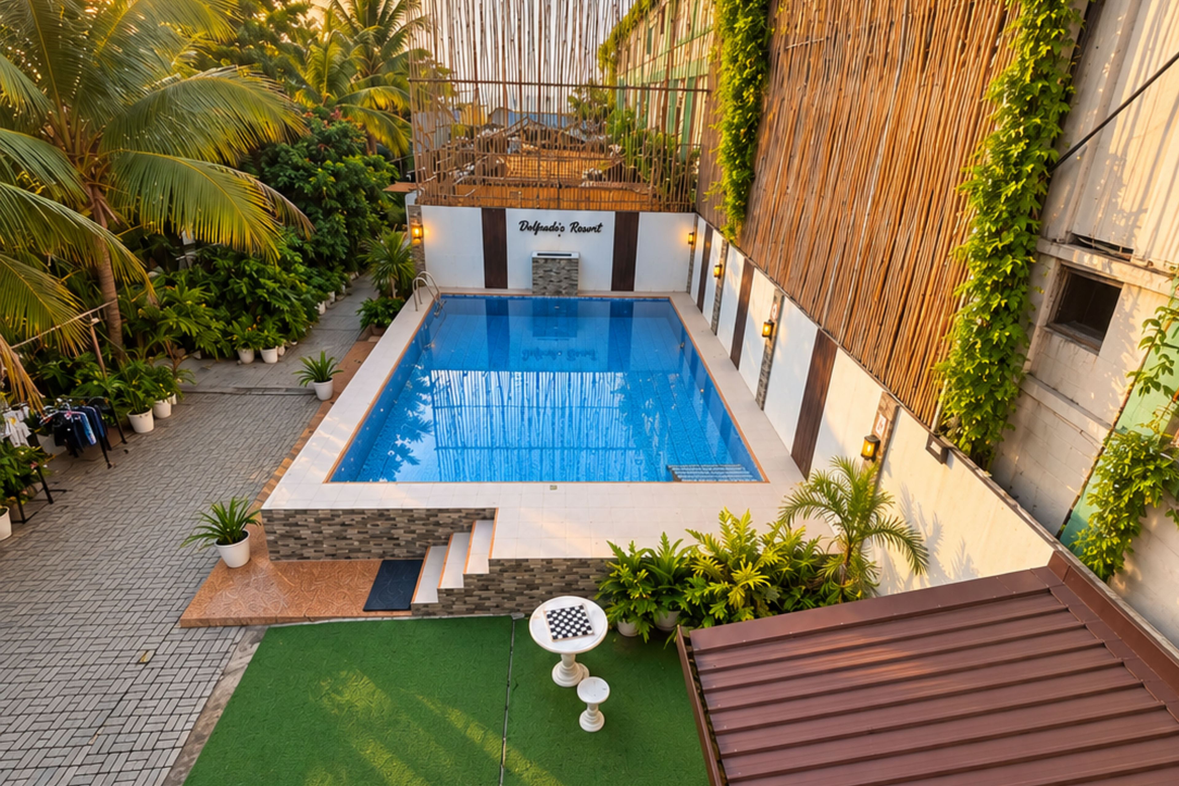 A rooftop swimming pool with a view of the city, surrounded by greenery and a bamboo fence.