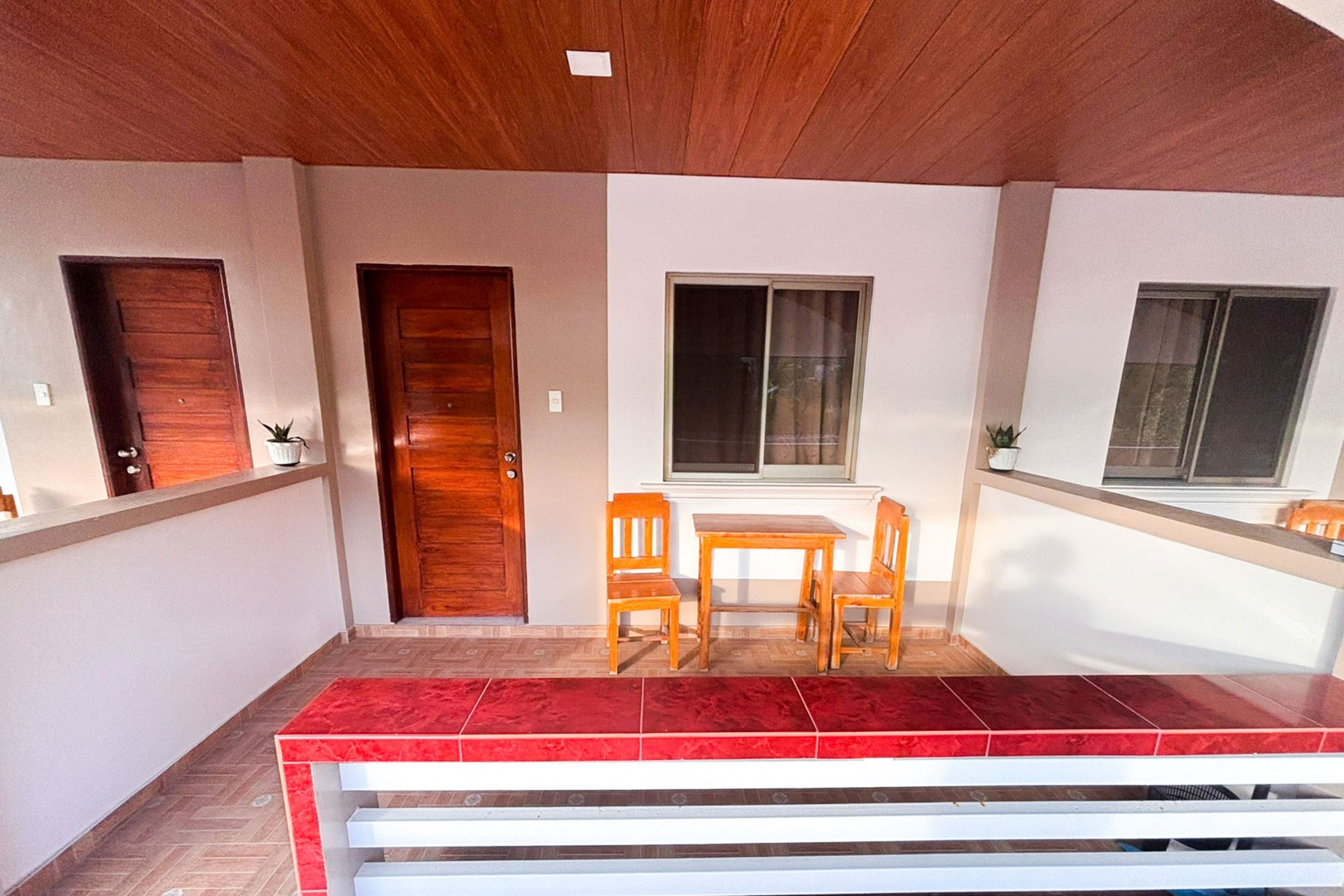 Una stanza con una porta in legno, una finestra, un tavolo con sedie e una zona tappezzata di moquette rossa.