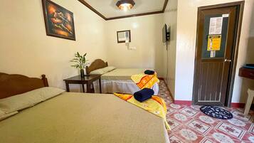 Une chambre d’hôtel avec deux lits, une petite table avec une plante, un tableau au mur, un avis sur la porte et des carreaux de sol à motifs.