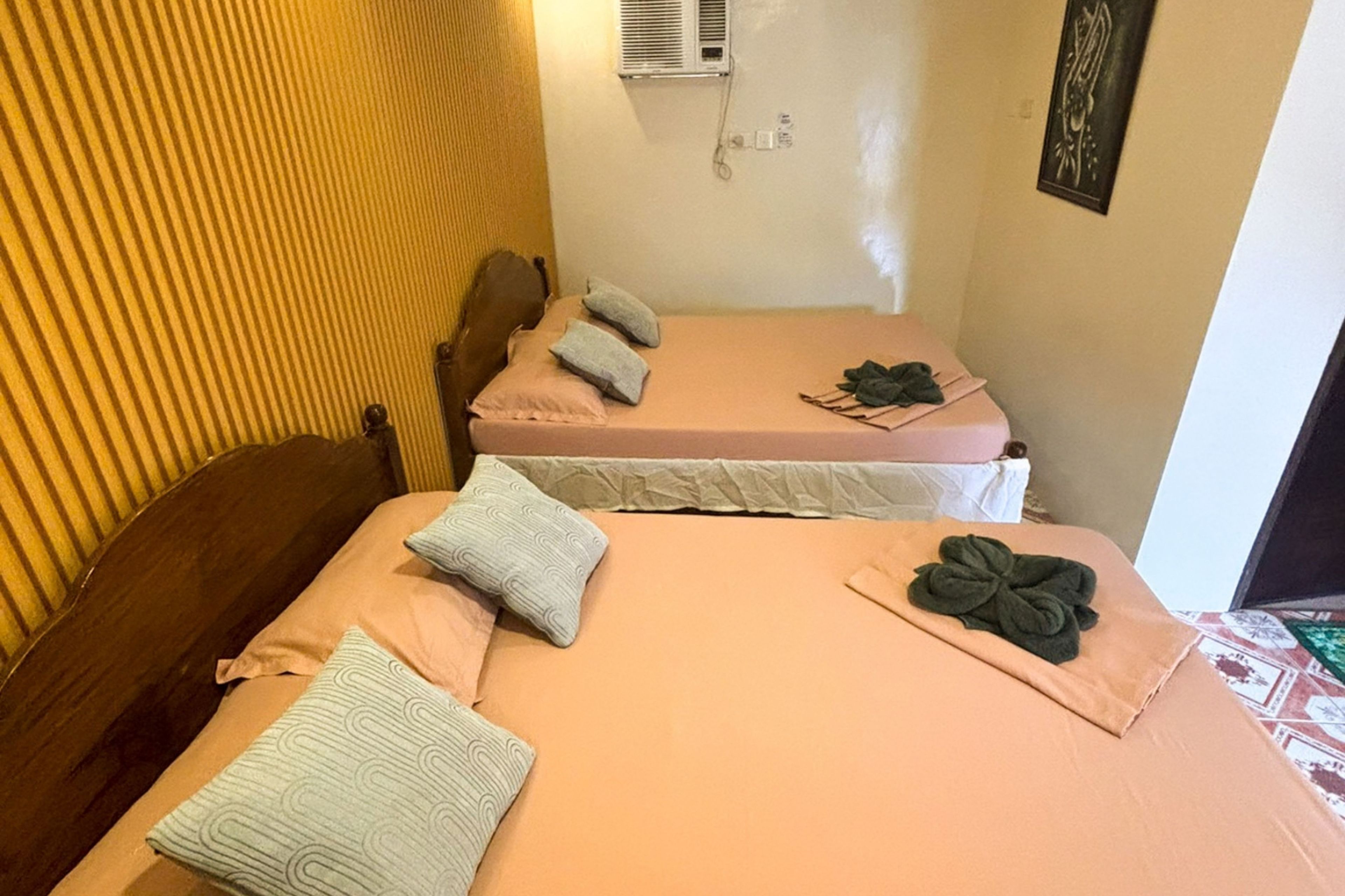 Una habitación con dos camas, cada una con una colcha y almohadas rosadas, un cabecero de madera y un aire acondicionado instalado en la pared.