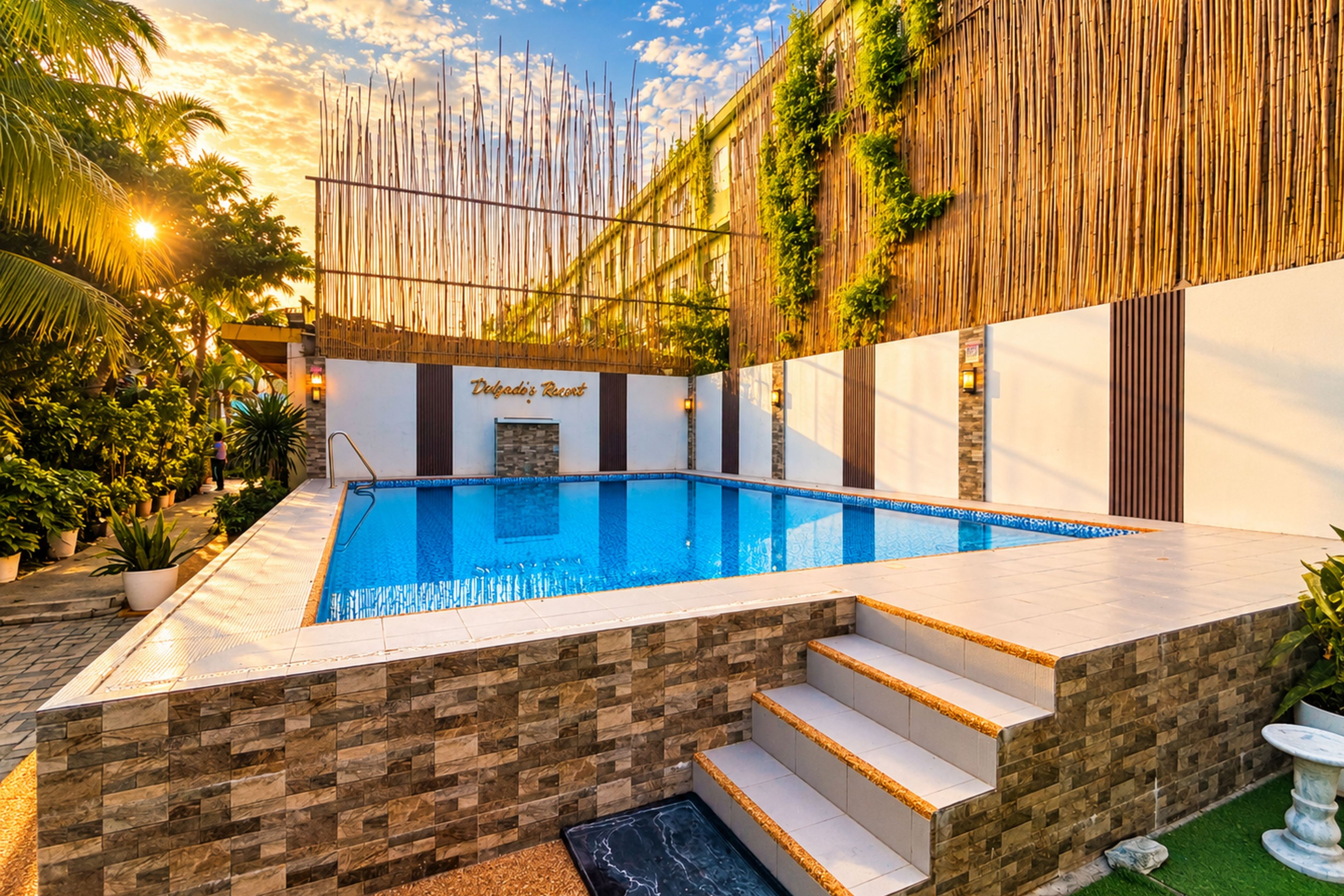 Una piscina con borde de baldosas de piedra, rodeada por una valla de bambú, y un cartel que dice 'Dulgado's Resort'.