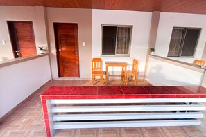 A room with a wooden door, a window with curtains, a small table with two chairs, and a red-tiled floor. - Delgados Resort Puerto Galera powered by Cocotel (Puerto Galera)
