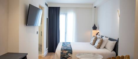 A modern hotel room with a large bed, a TV mounted on the wall, and a small round table.