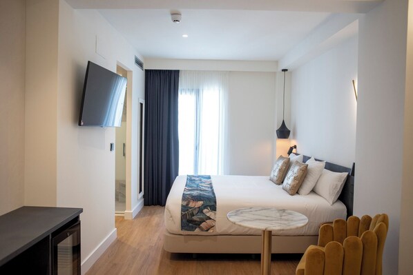 Quarto de hotel moderno com uma cama grande, uma TV fixada na parede e uma pequena mesa redonda.