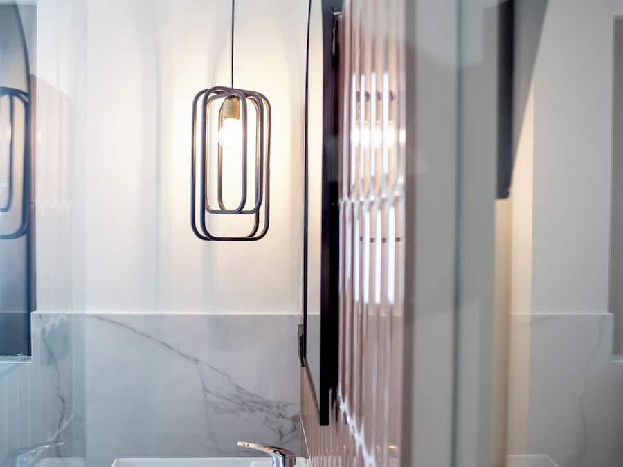 A modern bathroom with a marble sink, a glass enclosure, and a pendant light.