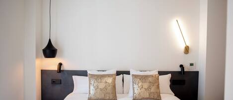 Una habitación de hotel moderna con una cama grande, dos mesitas de noche, una lámpara de pared y un termostato.