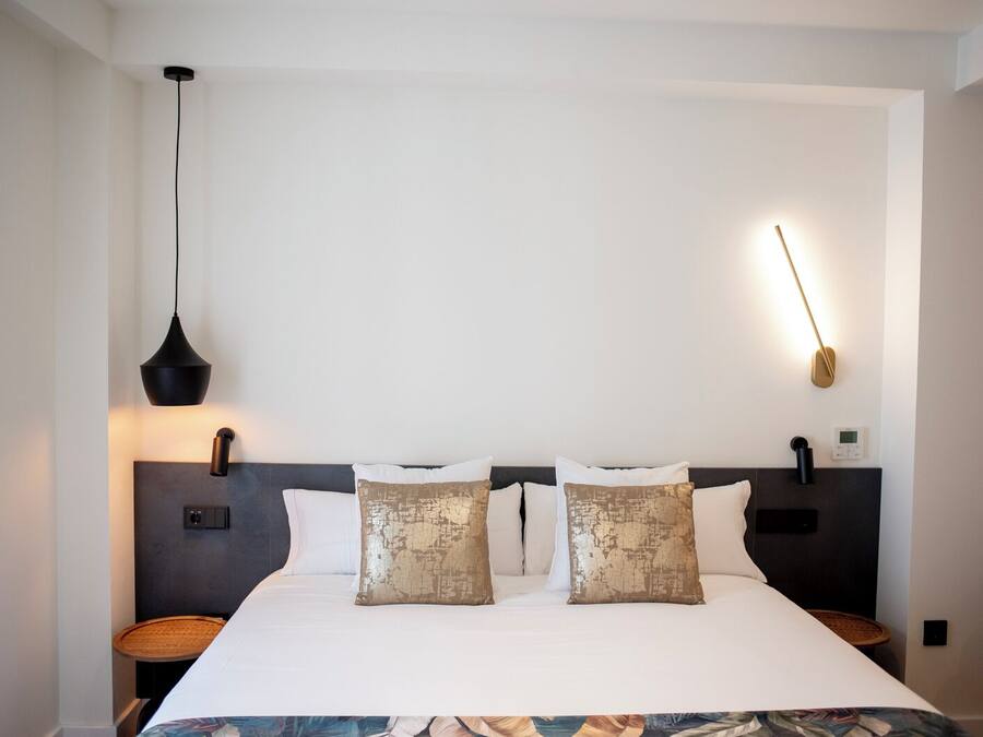 Una habitación de hotel moderna con una cama grande, dos mesitas de noche, una lámpara de pared y un termostato.