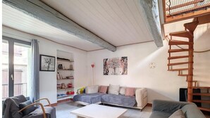 Un salon chaleureux avec un canapé, un fauteuil et une table basse. On y trouve une bibliothèque, un tableau et une échelle en bois.