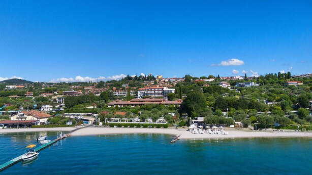 A coastal town with a marina, sandy beach, and residential buildings. - AHG Riva Del Sole Wellness Hotel - Adults Only (Moniga del Garda)