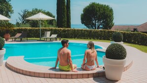 A couple sitting by a pool with a view of the sea, surrounded by potted plants and lounge chairs. - AHG Riva Del Sole Wellness Hotel - Adults Only (Moniga del Garda)