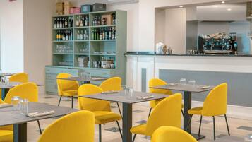 A restaurant with yellow chairs and tables, a bar area with a counter, and a shelf with various bottles.