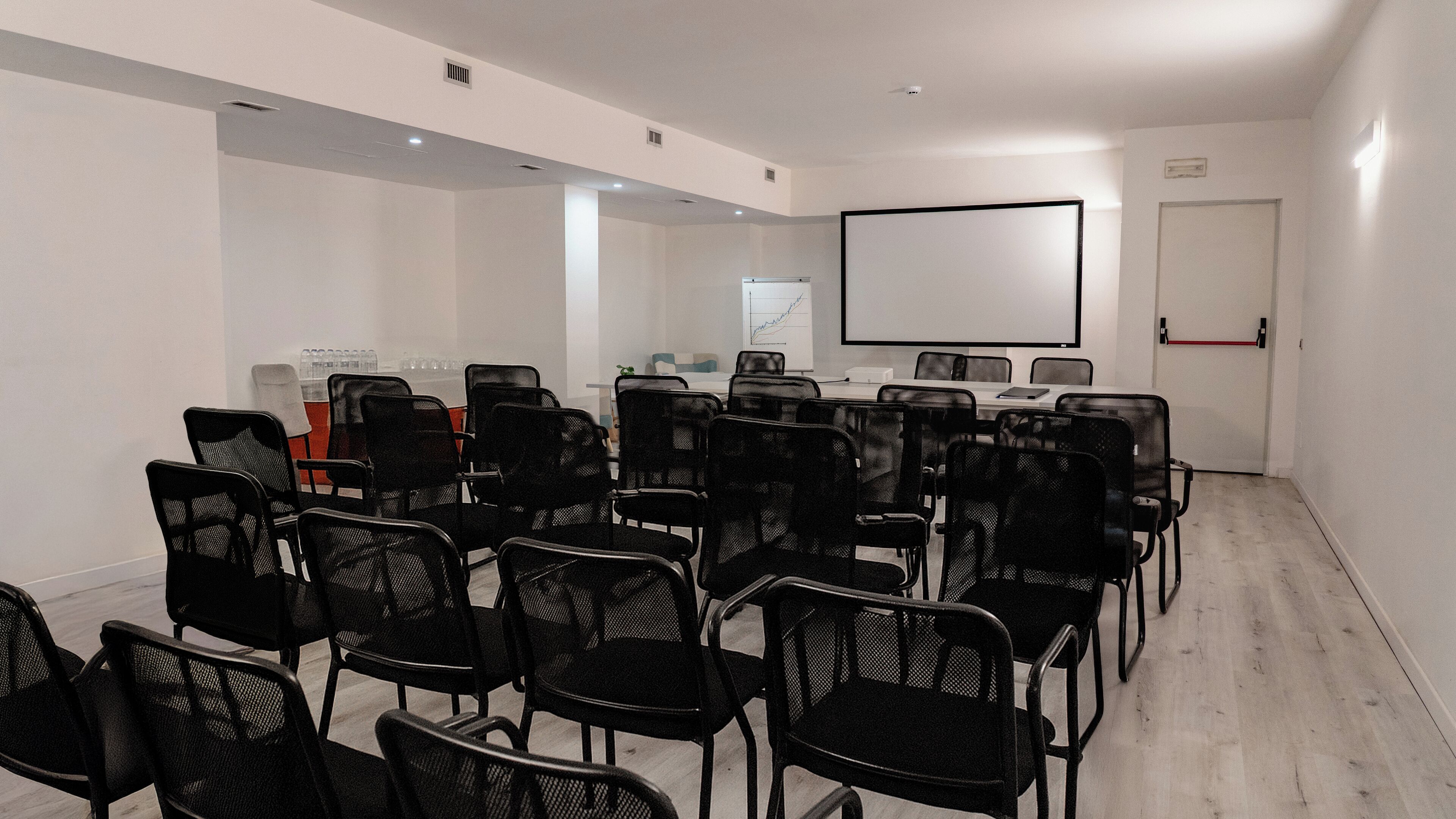 Ein Konferenzraum mit Reihen schwarzer Mesh-Stühle, einer Whiteboard und einer Projektionsleinwand.