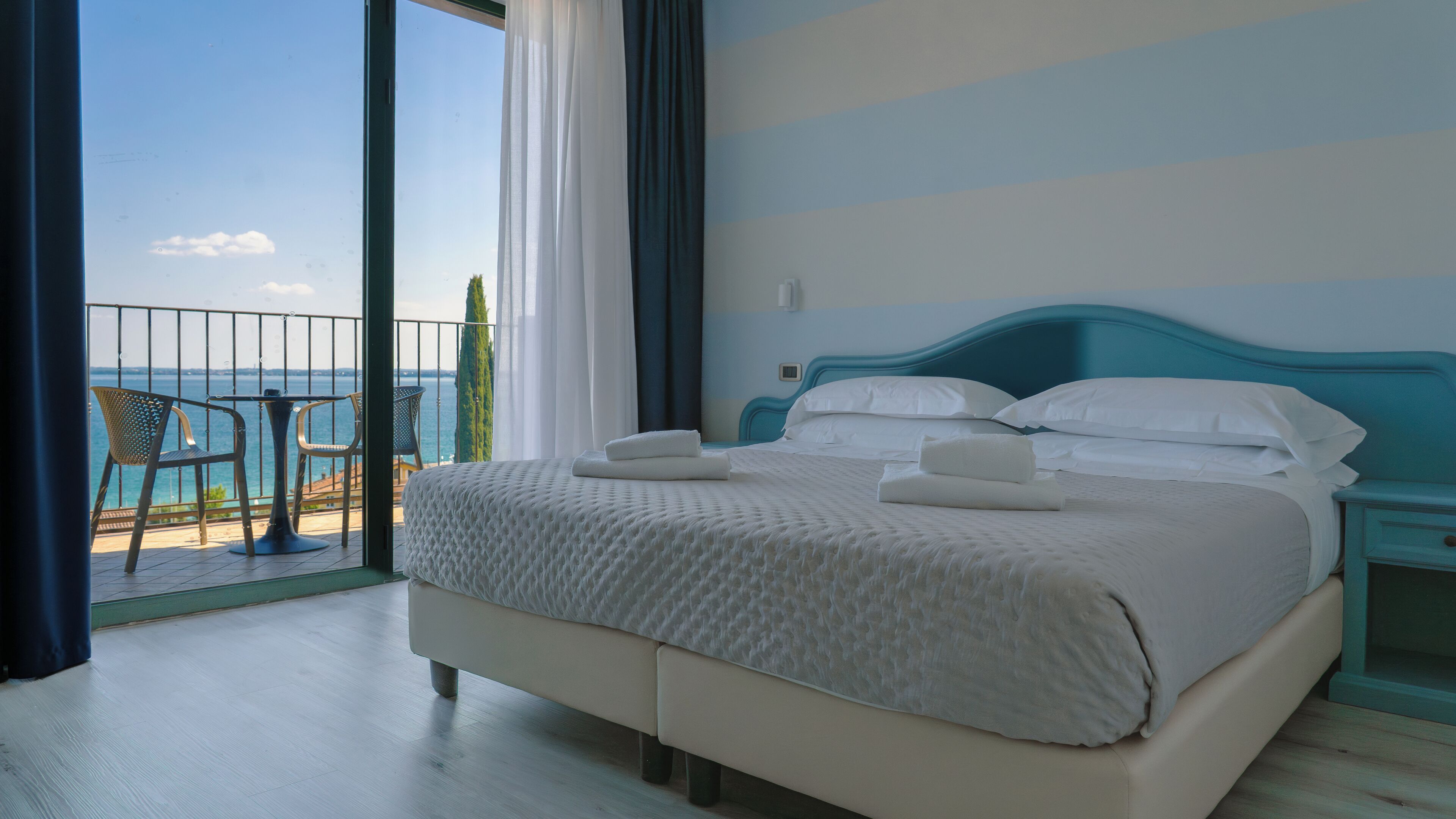 Habitación de hotel con cama, mesita de noche y vista al mar desde el balcón.