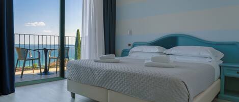 Quarto de hotel com cama, mesa de cabeceira e vista para o mar através de uma varanda.