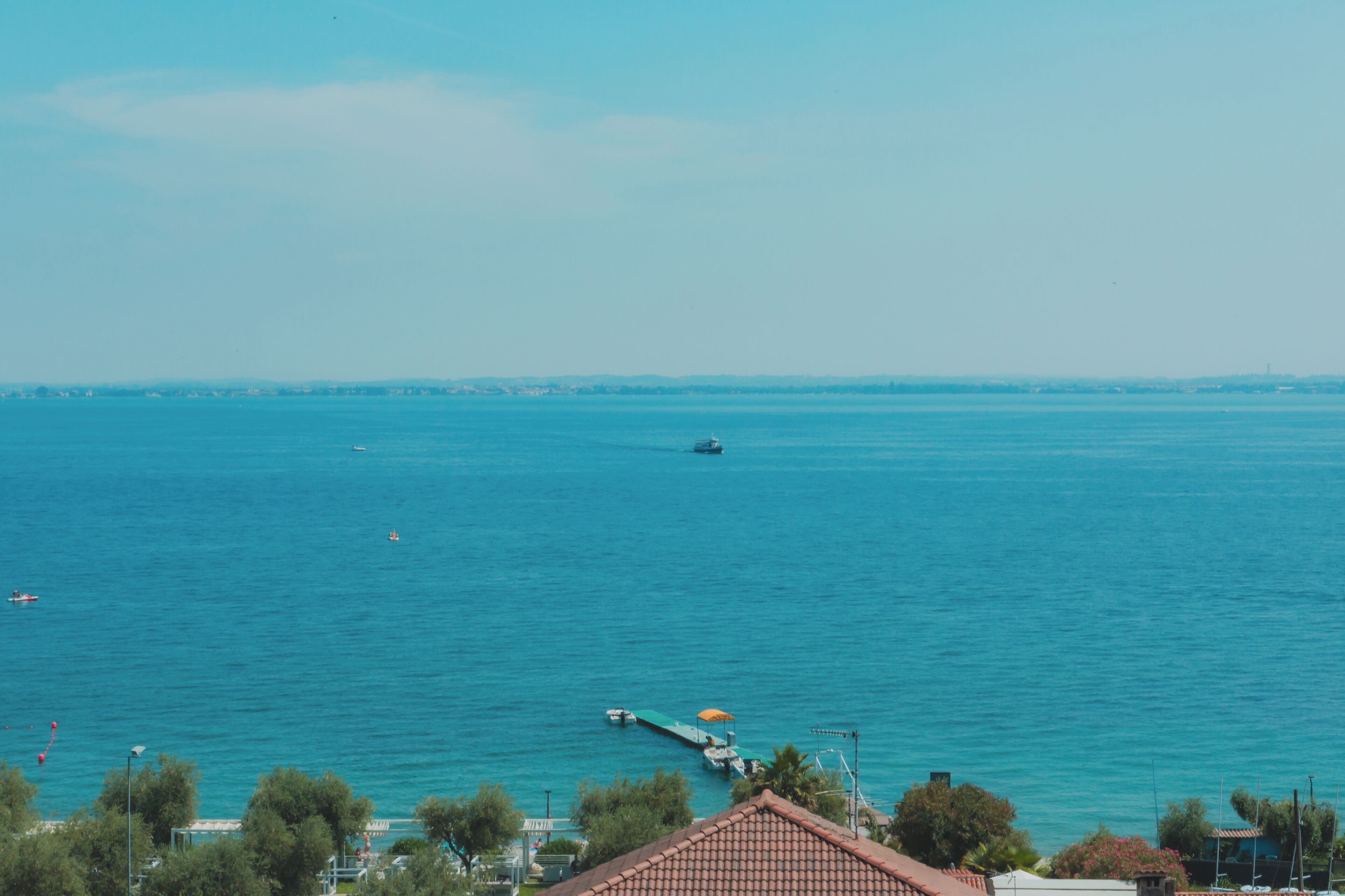 Vista costera con cielo despejado, mar tranquilo y un muelle con un barco.