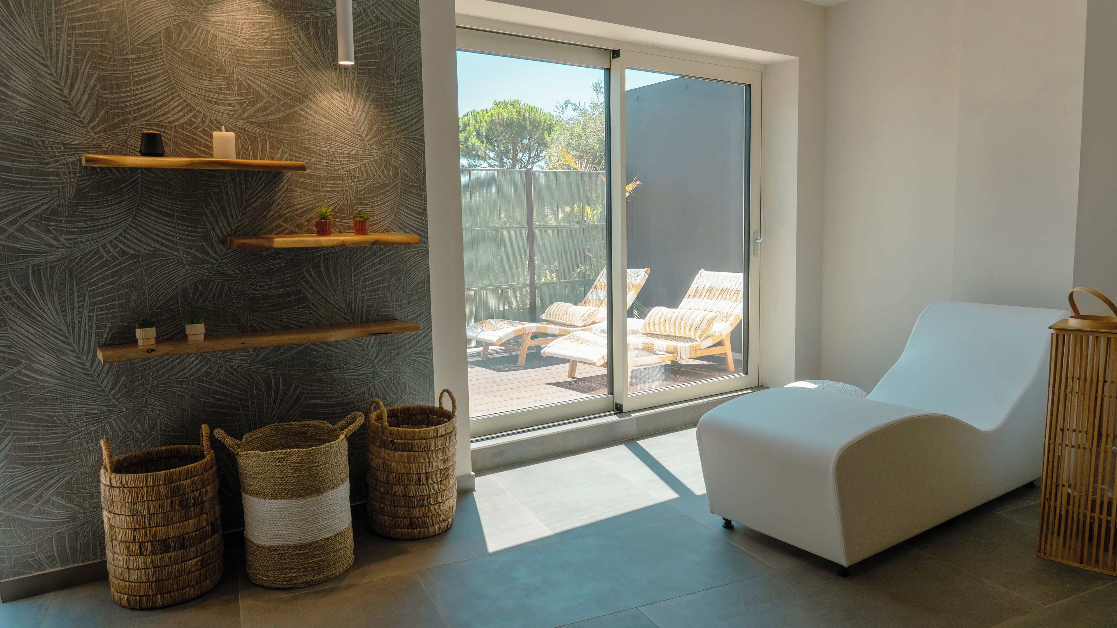A modern room with a sliding glass door leading to an outdoor area with lounge chairs. There are woven baskets and wooden shelves on the wall.