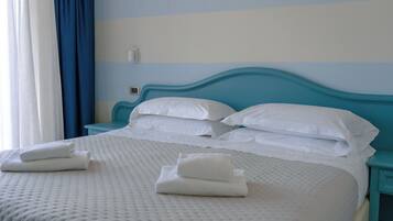 Una cama bien hecha con sábanas y toallas blancas, un cabecero azul y un termostato fijado a la pared.