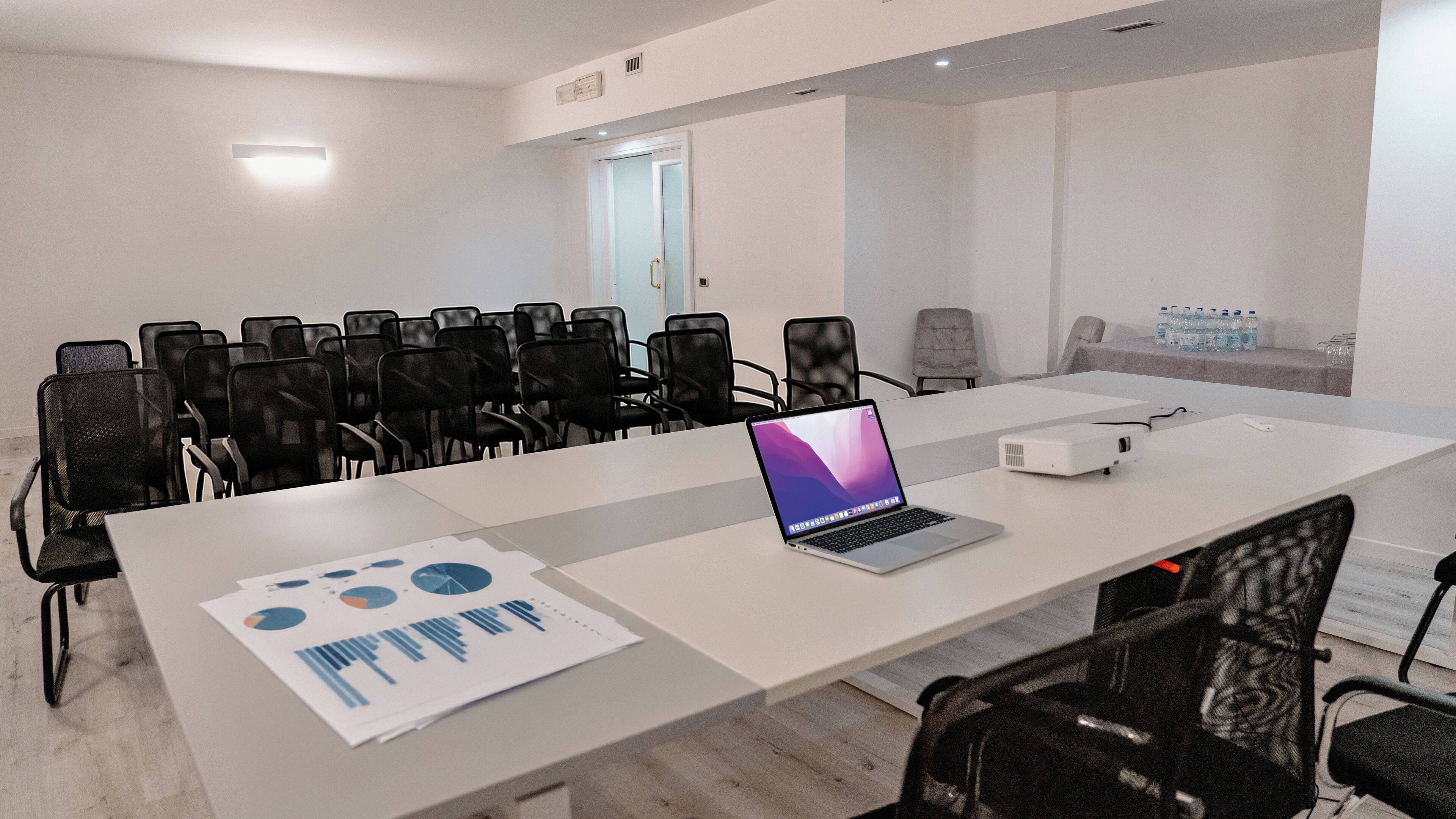 Une salle de conférence équipée d’une longue table, de plusieurs chaises, d’un ordinateur portable, d’un projecteur et de documents imprimés.