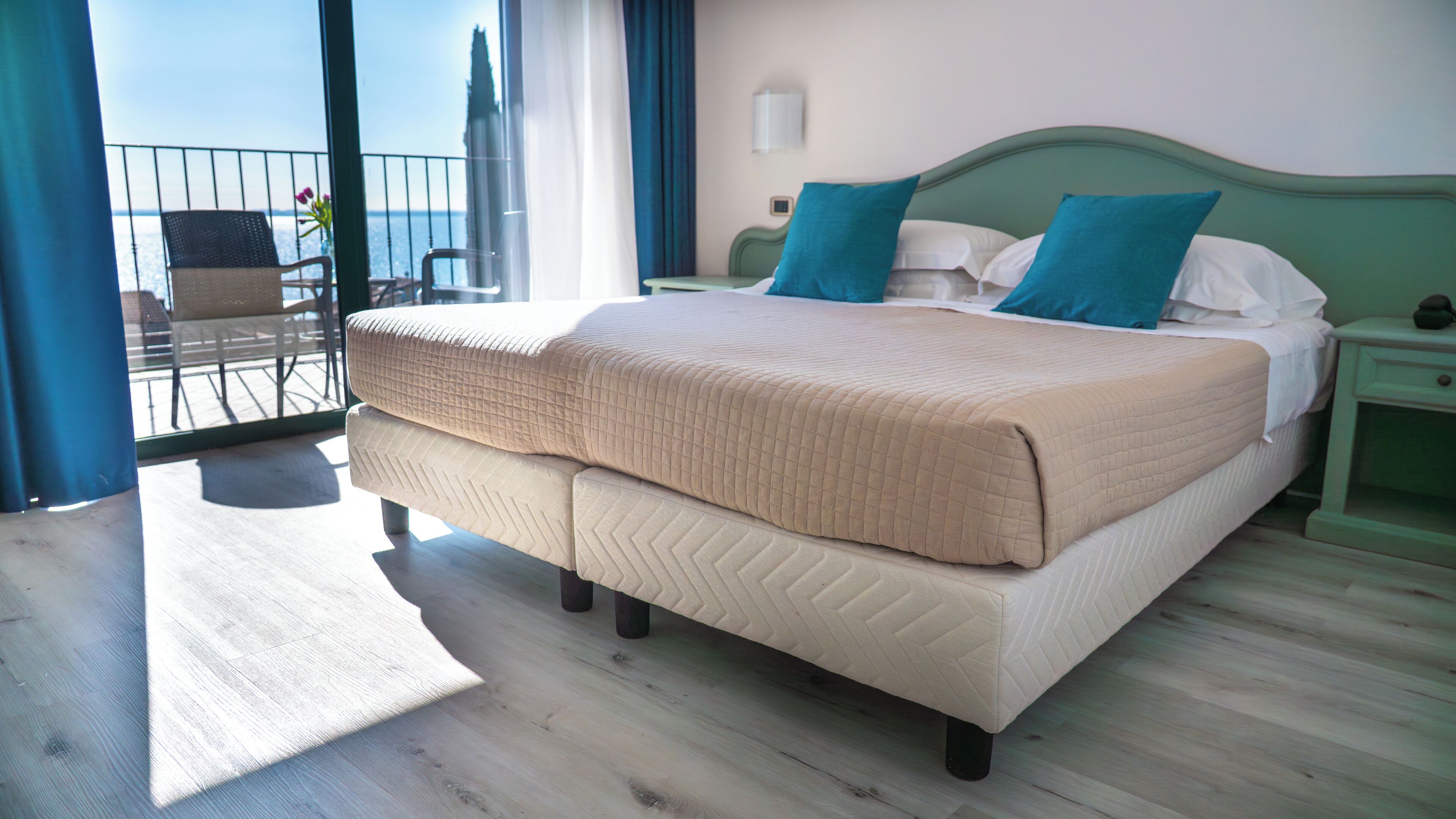 Camera d'albergo con un letto grande, una testiera verde e vista sul mare da un balcone.