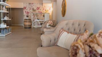 A living room with a beige sofa, a white coffee table, and a floral wallpaper. There is a white cabinet with glass doors on the left.