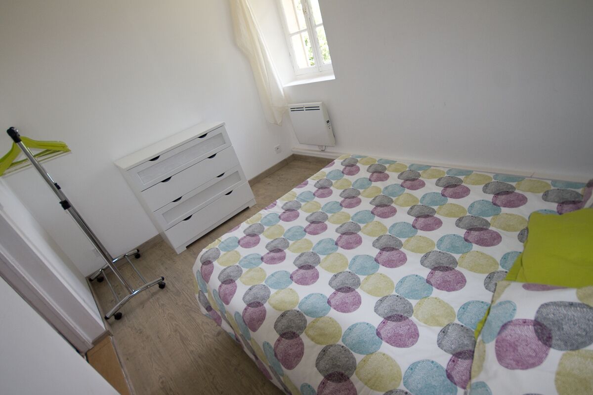 Un dormitorio con una cama, un aparador blanco, un radiador y una ventana con cortinas.