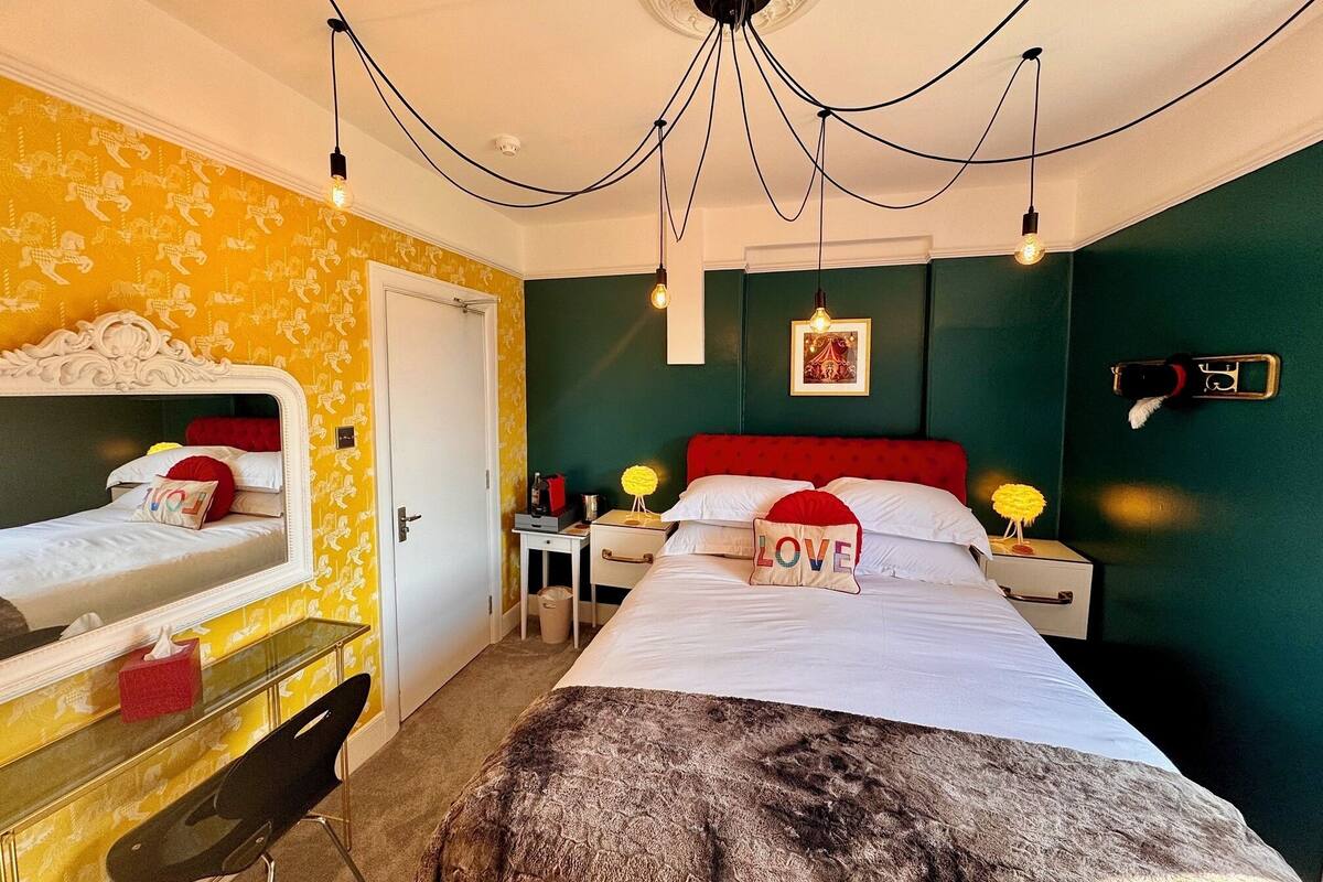 Een hotelkamer met een bed, nachtkastje, spiegel, wandlamp en een telefoon aan de muur.