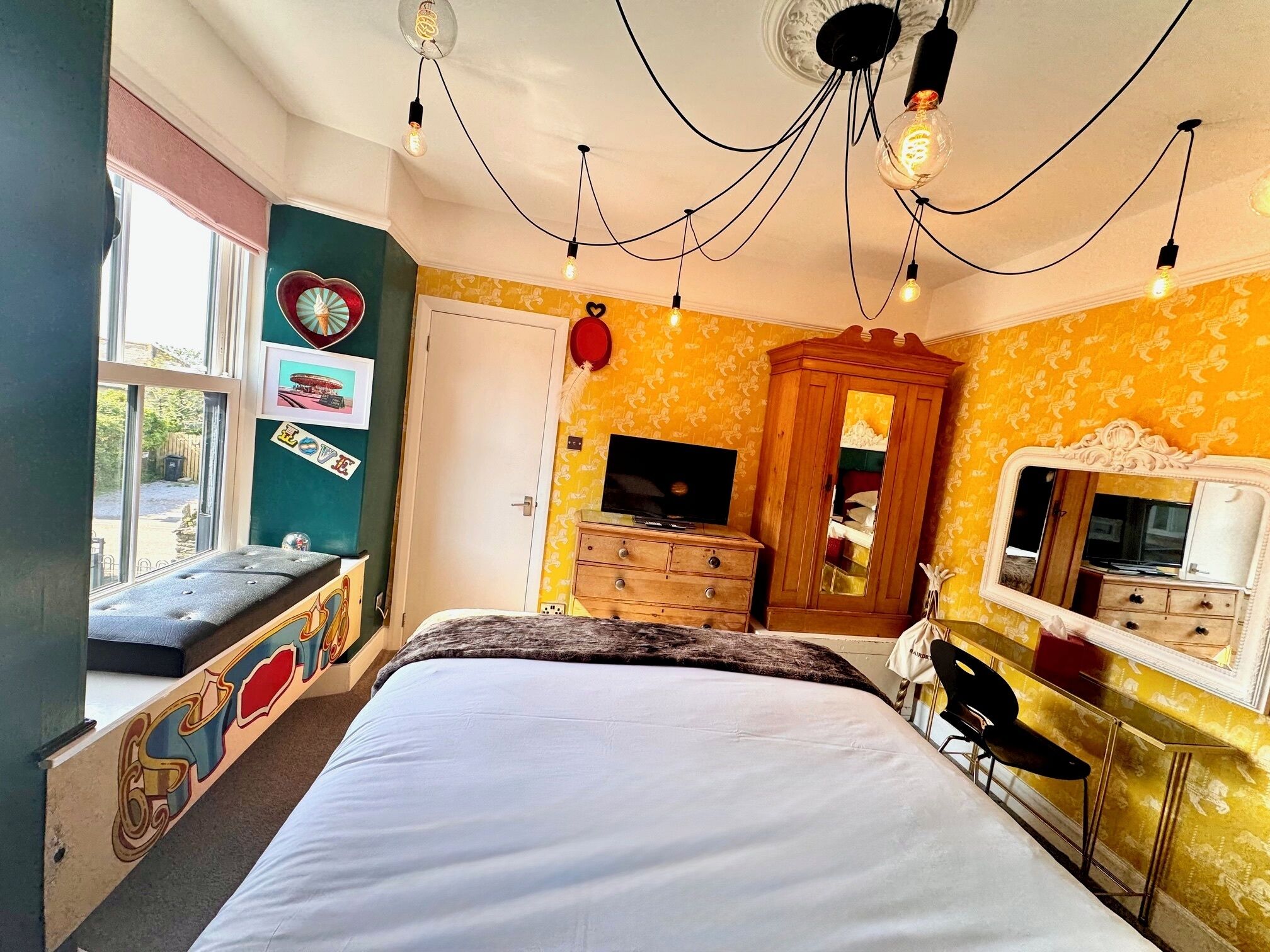 A bedroom with a bed, dresser, vanity, and a television.