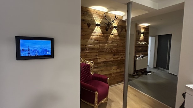 Un interior moderno con una pared de madera, un sillón tapizado en rojo y un televisor de pantalla plana mostrando un paisaje urbano.