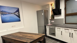 Una cocina moderna con horno empotrado, refrigerador y una mesa de madera con cojines a cuadros.