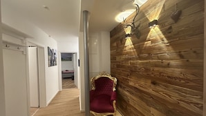 Un pasillo con pared de madera, un sillón de terciopelo rojo y una puerta que da a un dormitorio.