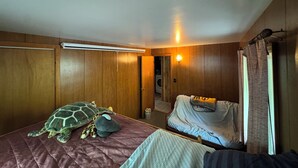 Een slaapkamer met houten wanden, een bed met een geborduurde hoes, een zacht knuffeldier in de vorm van een schildpad en een wasmachine op de achtergrond.