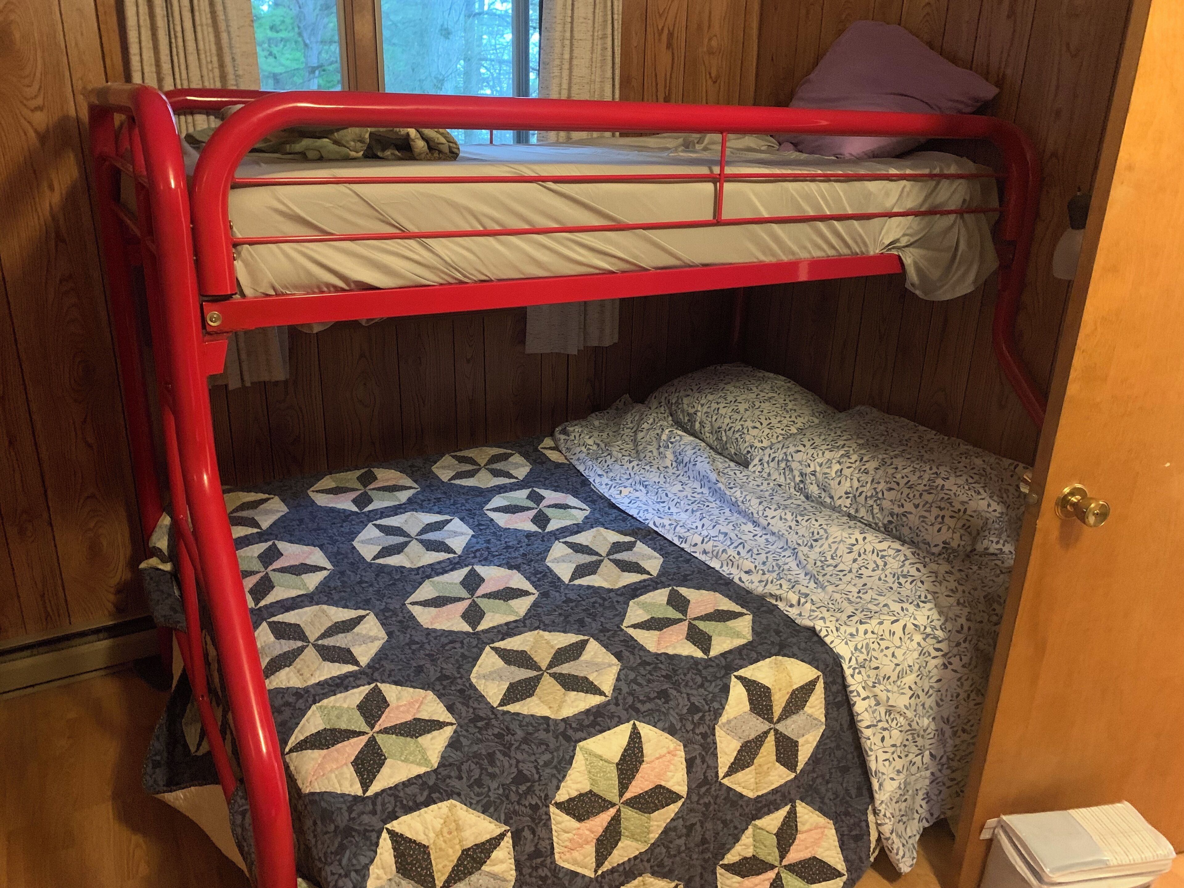 A bunk bed with a geometric patterned bedspread and a plain mattress on the top bunk.