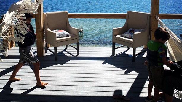 Een houten terras met twee stoelen en een hangmat, met uitzicht op een waterpartij.