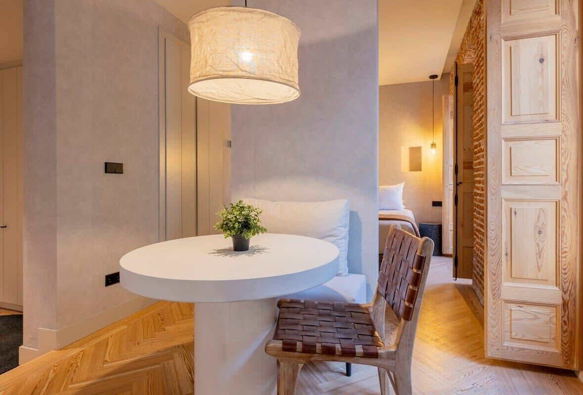 Une chambre d’hôtel moderne avec une table ronde, un banc, une plante en pot et une grande porte en bois.
