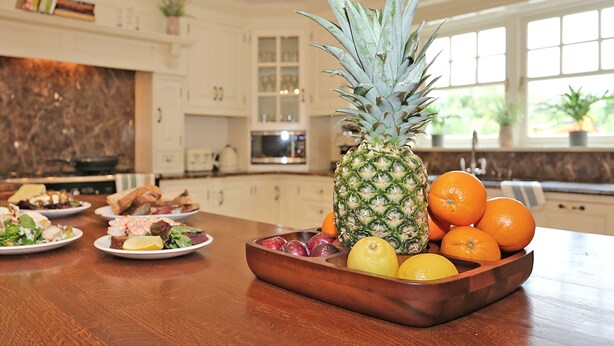 A kitchen with a wooden table displaying food, a pineapple, and oranges. - Luxury Manor Private Cinema, Bar, Games & Music Rooms. Perfect for Large Groups (Limerick)