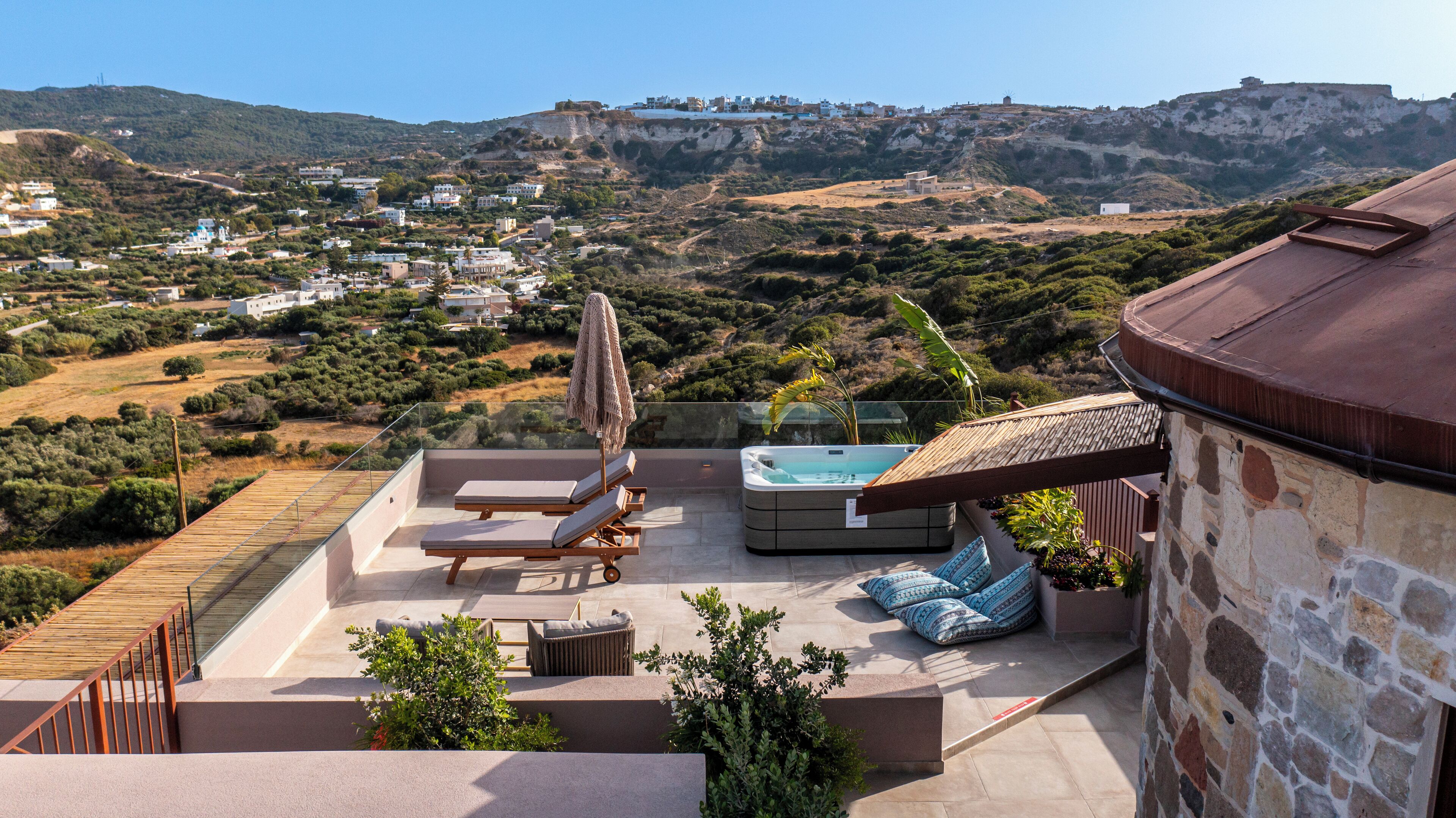 A rooftop terrace with a hot tub, lounge chairs, and a view of a hillside town.