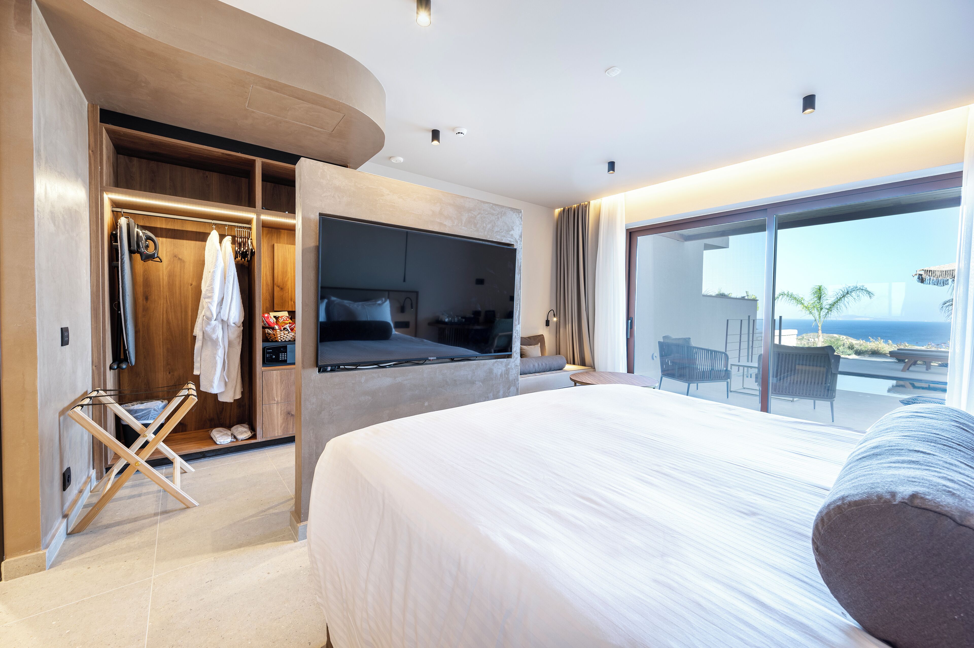 A modern hotel room with a large bed, a walk-in closet, and a balcony with a view of the ocean.