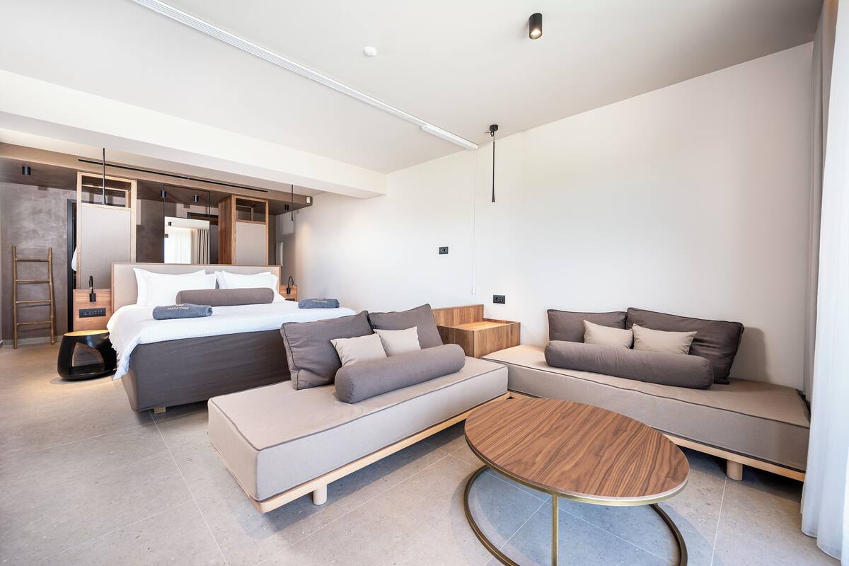 A modern hotel room with a large bed, two sofas, a small round table, and a walk-in closet.
