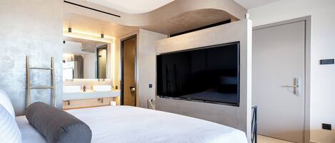 A modern hotel room with a large bed, a TV mounted on the wall, a bathroom with a vanity, and a door with a handle.