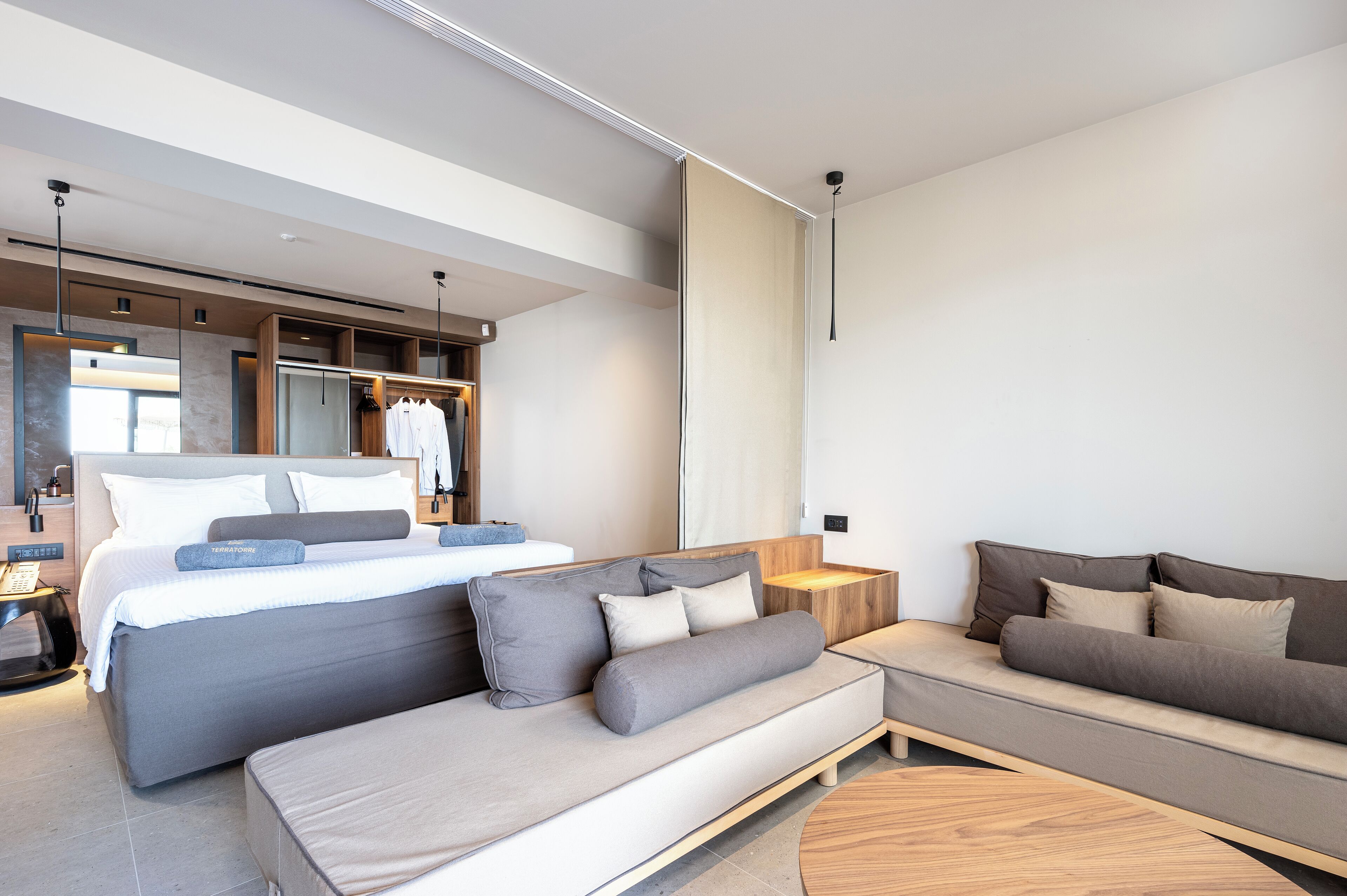 A modern hotel room with a large bed, a sofa, a small table, and a mirror.