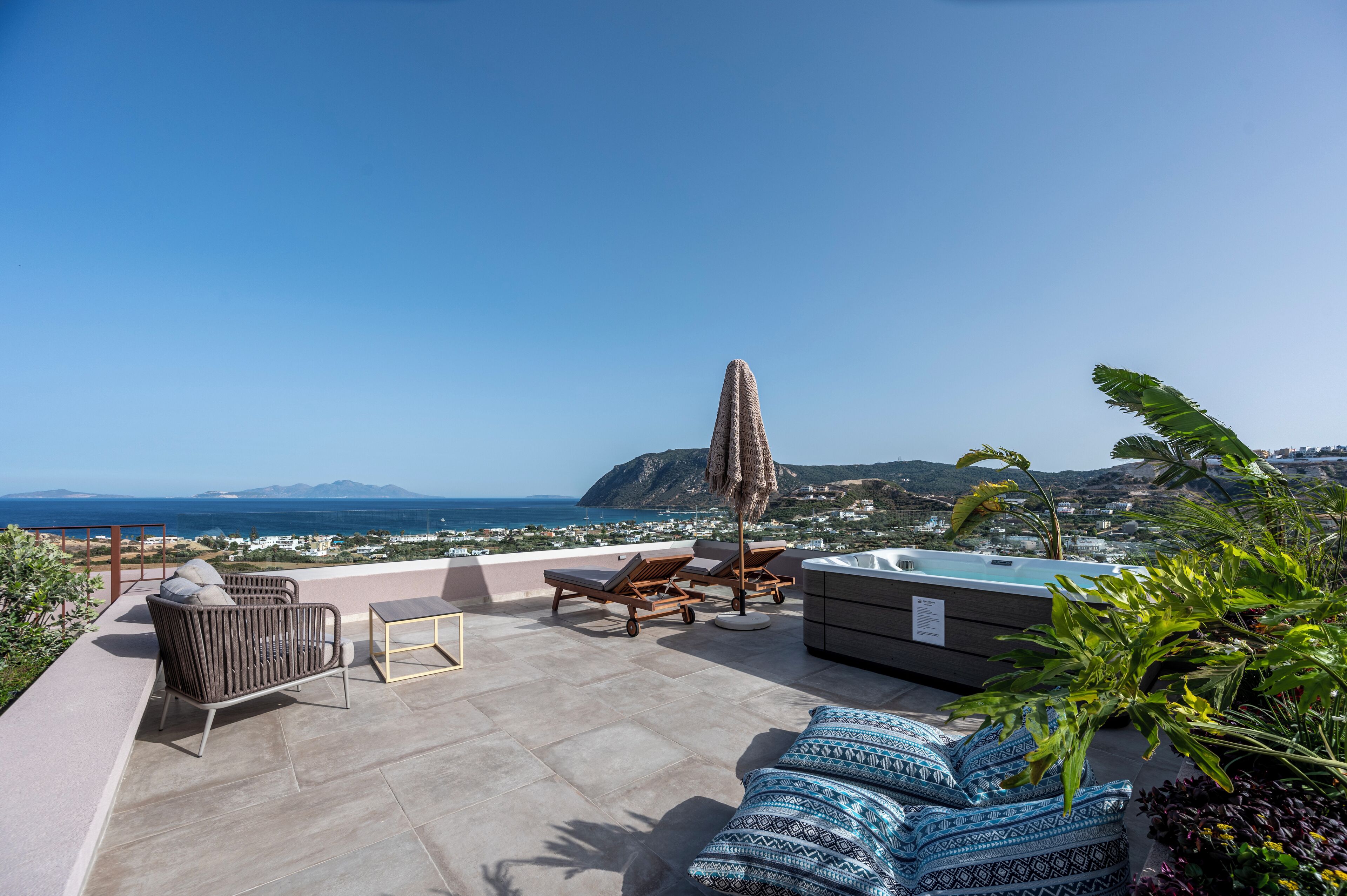 A rooftop terrace with lounge chairs, a hot tub, and a view of the ocean.