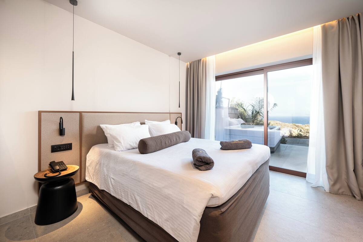 A modern hotel room with a large bed, a bedside telephone, and a view of the outdoors.