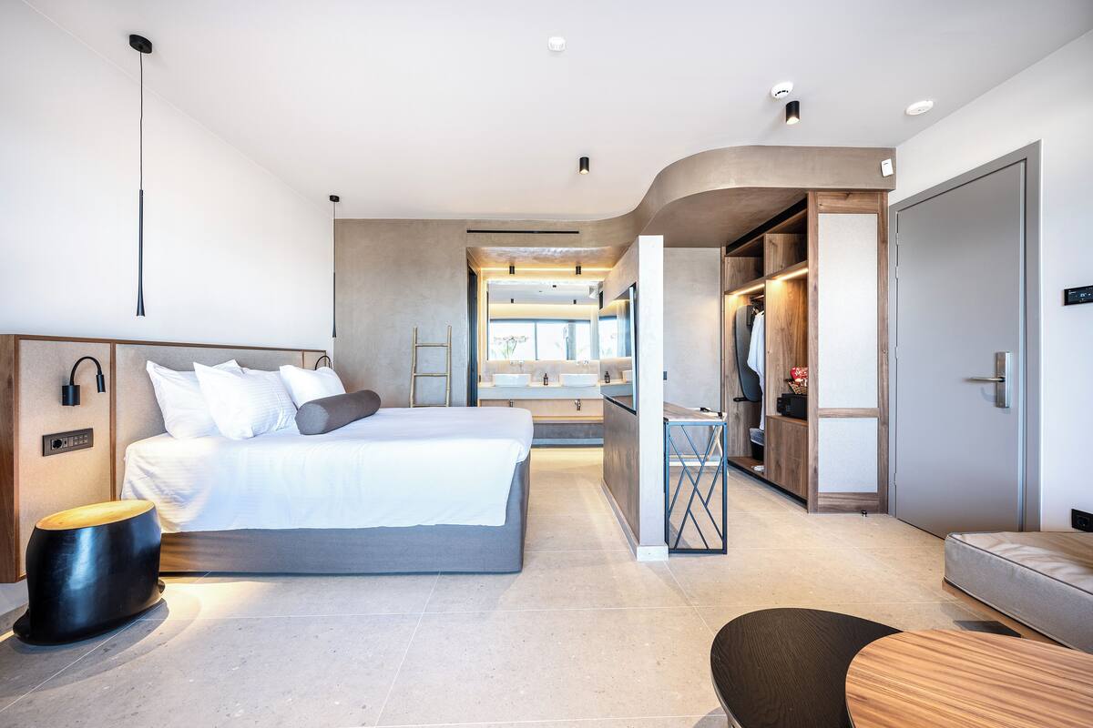 A modern bedroom with a large bed, bedside tables, a wardrobe, and a bathroom visible through an open door.