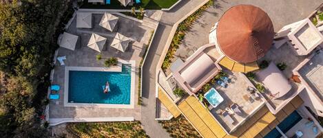 An aerial view of a resort with a swimming pool, sun loungers, and a hot tub.